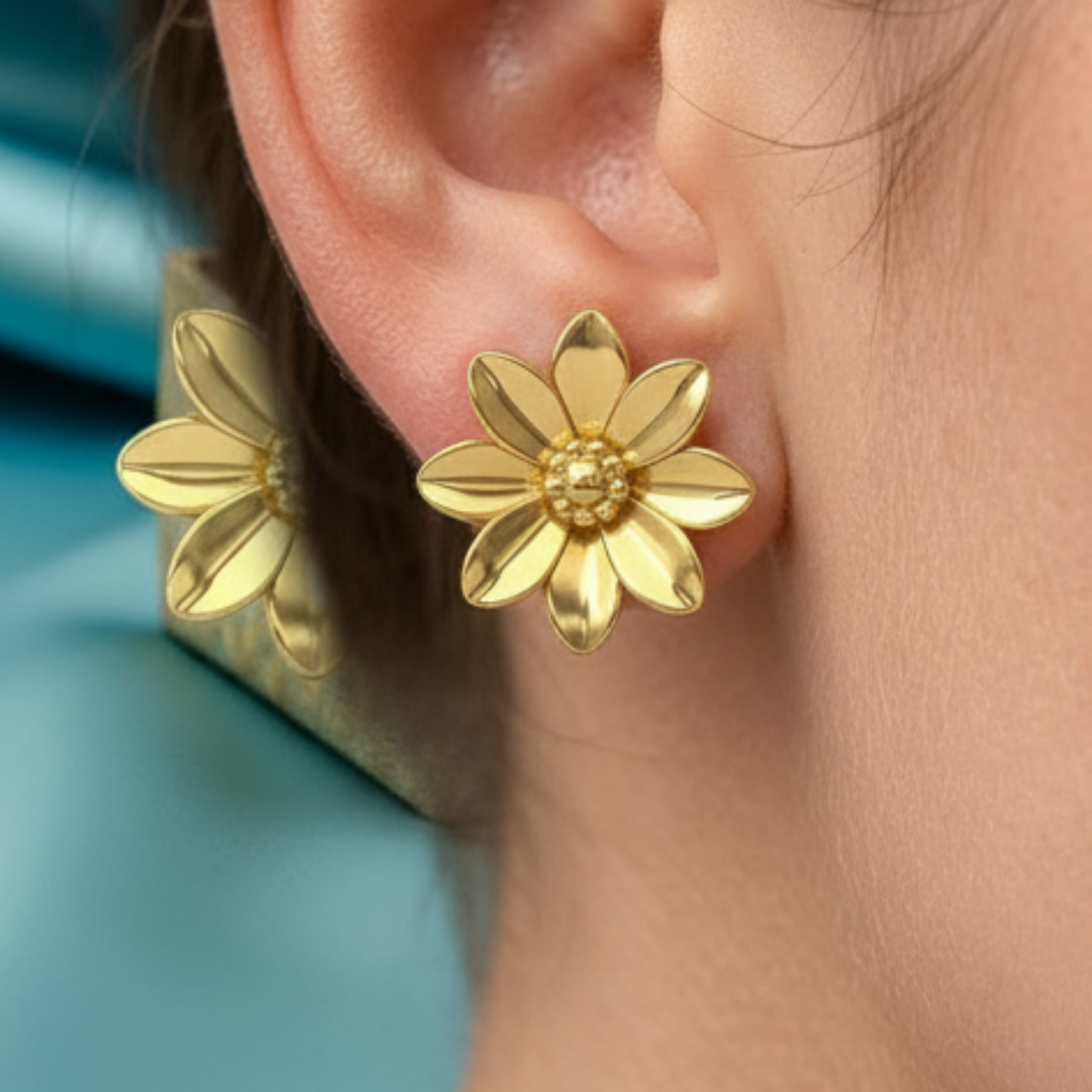Polished Brass Flower Stud Earring by MokshaGoldSculptures, handmade with detailed petals, worn against a blue-green background.
