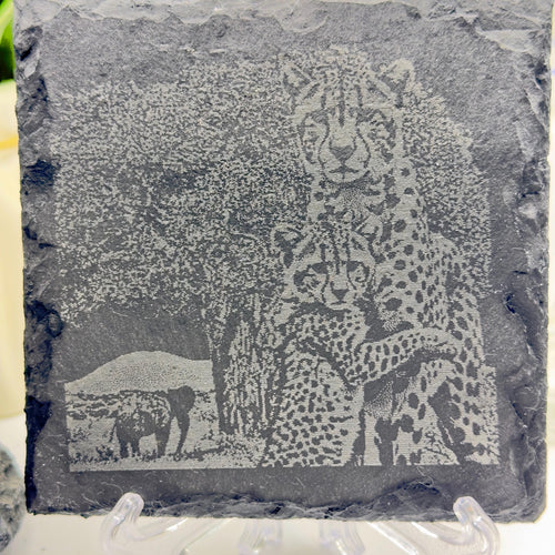 The Cheetah Cub Hugging Mother slate coaster by MokshaGoldSculptures with engraved cheetahs, elephants, and trees.