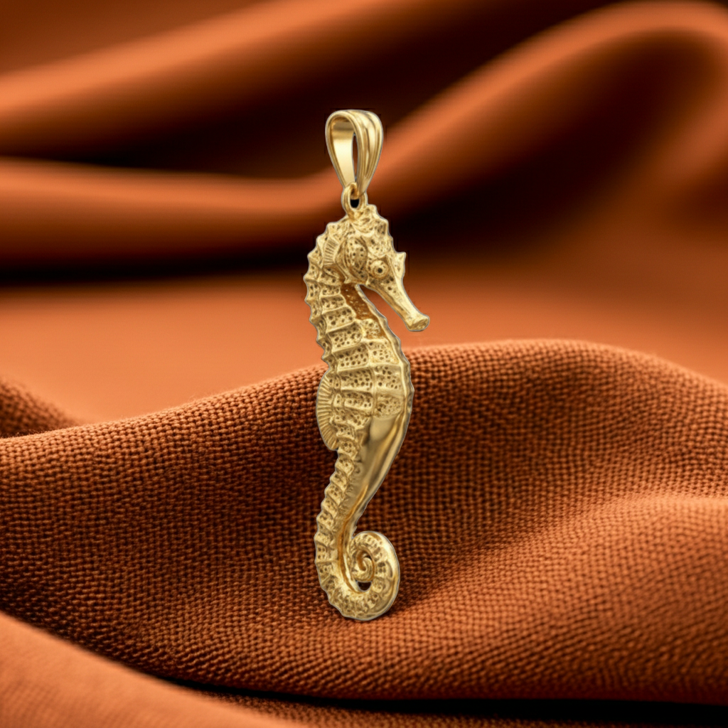 The Seahorse Pendant Necklace in gold, silver & brass by MokshaGoldSculptures on soft brown fabric.