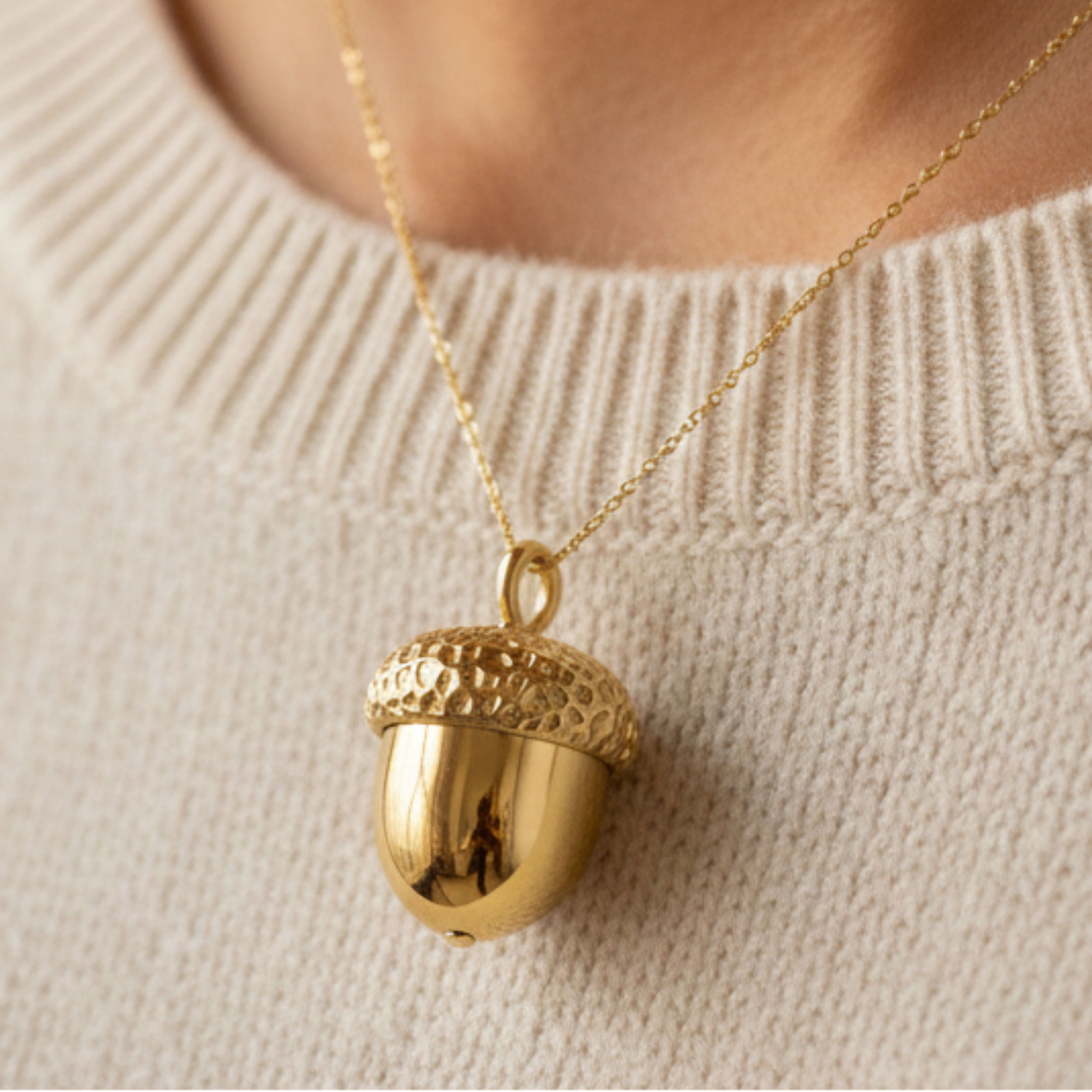 The Gold Acorn Pendant Necklace in 24K gold plate by MokshaGoldSculptures displayed on a cream knit sweater.